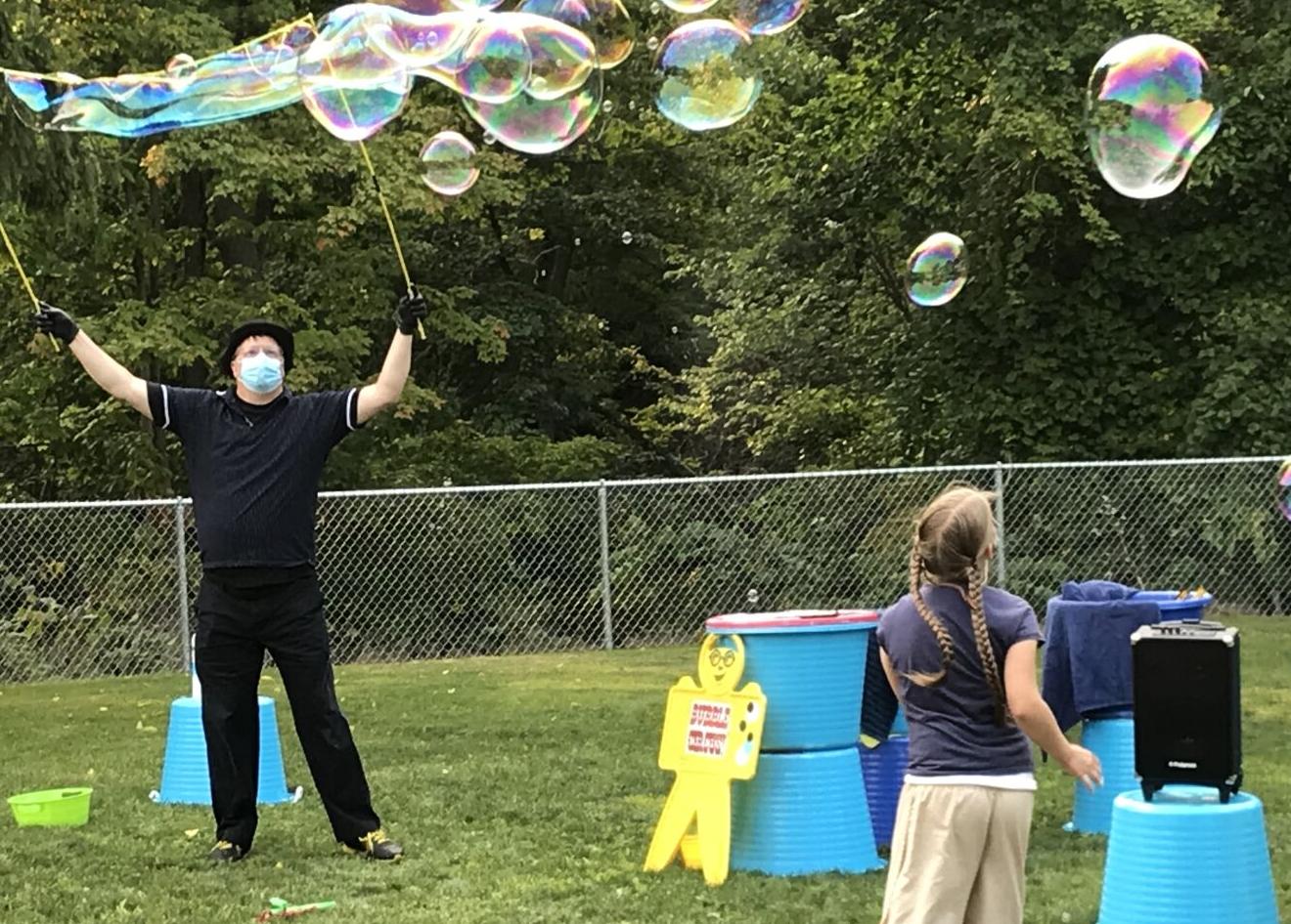 Rayna Gingerich (bottom right) and performer Doug Rougeux (left of center) play with bubbles at the library’s summer reading program celebration.